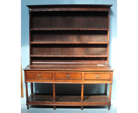 An 18th century oak dresser, the shaped cornice above a planked back with three shelves, over a base of three short frieze dr