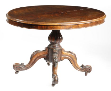 λ A Victorian rosewood loo table, the oval tilt-top on a lobed baluster stem, on flower carved cabriole legs and ceramic cast