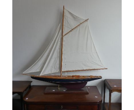 A vintage wooden Pond Yacht, the hull painted in red and blue, with canvas sails and metal fittings, on display stand, 103cm 