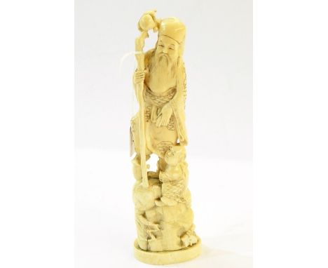 19th century Japanese carved ivory group of elderly man with wooden staff and attendant, on rockwork, the oval base carved ov