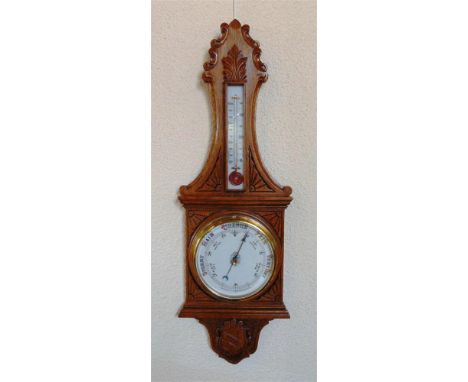 AN EDWARDIAN OAK ANEROIOD BAROMETER/THERMOMETER,  with carved decoration and eight inch ceramic dial, 90cm high overall