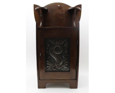 An Arts &amp; Crafts oak cabinet, the single door inset on ebonised metal panel, with stylised dolphin decoration, having ups