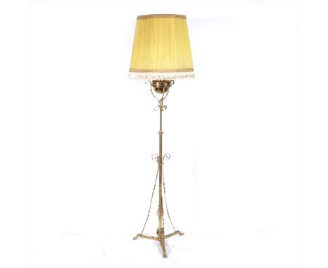 An Edwardian brass standard oil lamp, adapted for electricity, plain reservoir, tripod base, with shade 183cm overall.