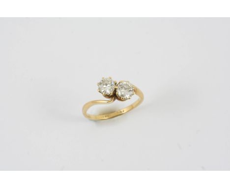 A DIAMOND TWO STONE CROSS-OVER RING set with two brilliant-cut diamonds in 18ct gold and platinum. Size K 1/2