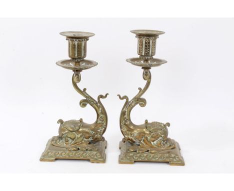 Pair of late 19th century brass desk candlesticks each with stylised dolphin support with integral inkwell, raised on square 