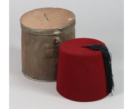 A vintage eastern red fez hat, with a tin cylindrical hatbox. 