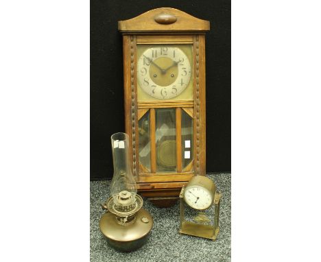 An early 20th century oak cased wall clock, pendulum and key; a brass portico type mantel clock; a brass Veritas oil lamp (3)