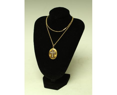 A Victorian gold coloured metal oval locket, applied with a blue enamel and seed pearl cross, engraved and chased with foliat