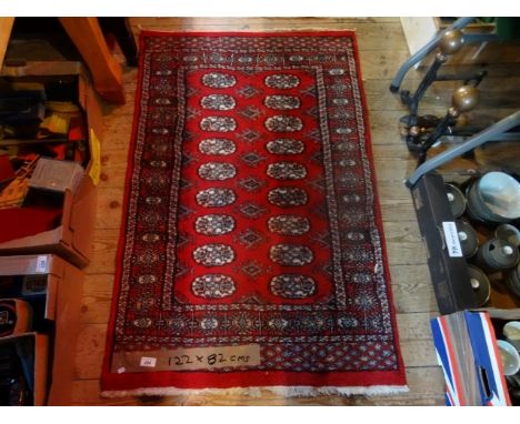 An Eastern carpet, having red central field bordered by geometric patterned shapes (122cm x 82cm). Condition Report: Good con