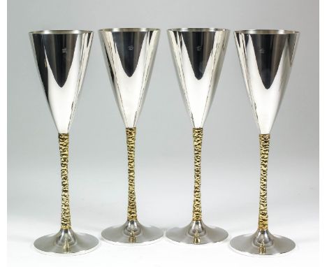 A set of four Elizabeth II silver and silver gilt champagne flutes, the plain conical bowls with textured silver gilt stems a