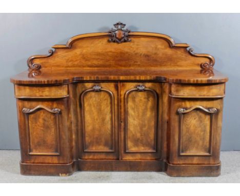 A Victorian mahogany break front sideboard, the shaped and moulded back with cartouche scroll and leaf carved cresting, fitte