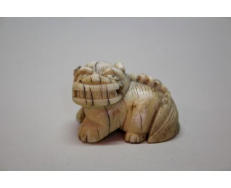 A Japanese carved ivory netsuke of a lion dog, Meiji period, 4.1cm long; together with a Japanese carved ivory netsuke of a b