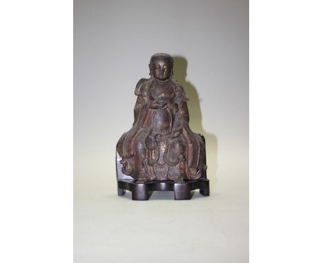 A Chinese bronze buddha, probably Ming, in seated position, with remains of red paint and gilding, on hardwood chair form sta