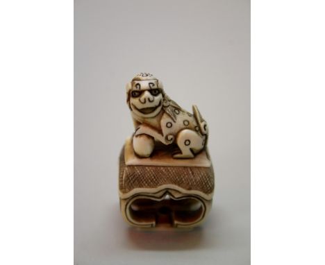 A Japanese carved ivory seal type netsuke of a shishi on a table, signed, 19th century, 4.5cm high.Provenance: purchased from