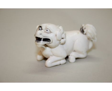 A Japanese carved ivory netsuke of a recumbent lion dog, signed, 5cm long.