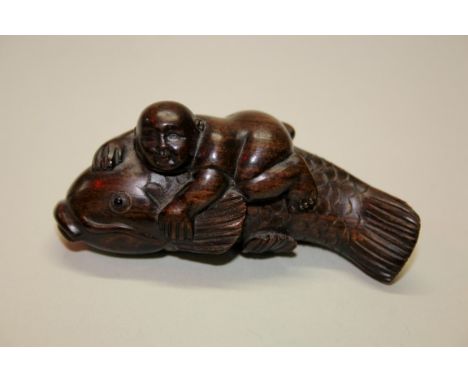 A Japanese carved hardwood netsuke of a boy on a carp, early 20th century, with signature tablet and inset eyes, 7cm long.Pro
