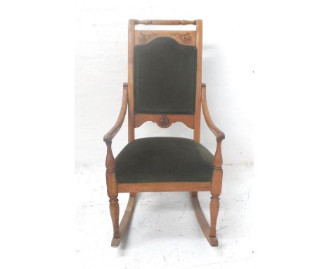 LIGHT OAK ROCKING CHAIRwith a turned spindle top rail above a shaped padded back with carved motifs and outswept arms above a