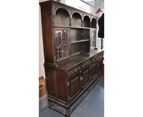 An oak sideboard, with galleried upper shelf, astral glazed outer sections, over four drawers with carved trefoil decoration,