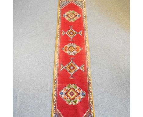 A Moroccan runner, with coloured diamond design, on a red ground, 339 x 72cm