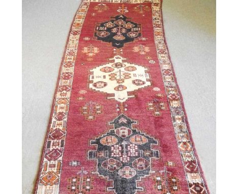 A Persian runner, with three hooked medallions, on a red ground, 410 x 145cm