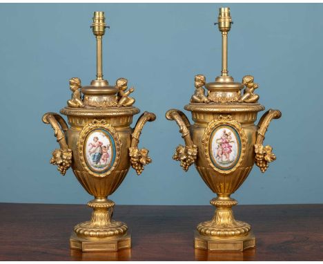 A pair of gilt metal table lamps in the form of classical urns, the handles with fruiting vine ornament, inset with porcelain