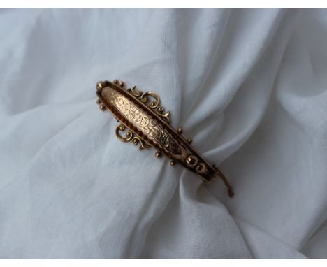 A 9ct yellow gold hinged bangle with a leaf engraved panel and ball and scrolls, marked 9ct, approximately 9 grams