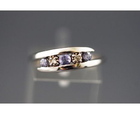 A white metal crossover ring set with tanzanites and diamonds. Stamped 10K and tested as minimum 9ct gold. Size: M 1/2, 1.8 g