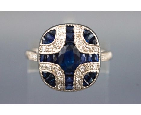 A white metal dress ring. Set with an oval faceted cut principal sapphire of approx. 0.61cts. Further set with graduated cali