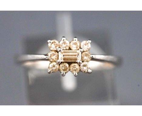 A white metal cluster ring set with a central baguette cut diamond and surrounded by round brilliant cut diamonds. Approx tot