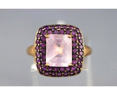 A yellow metal cluster ring set with a cushion cut pale amethyst and surrounded by round faceted cut amethyst. Hallmarked 9ct