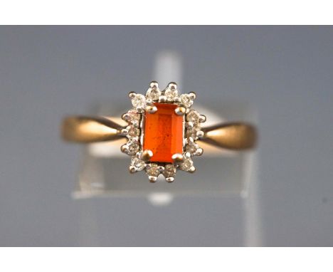 A yellow and white metal cluster ring. Set with a rectangular cut fire opal (untested) and surrounded by round brilliant cut 