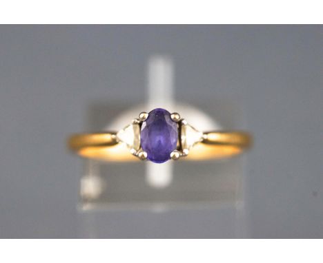 A yellow and white metal three stone ring set with an oval faceted cut tanzanite and flanked by brilliant cut diamonds. Hallm