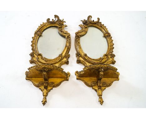 A pair of nineteenth century gilt framed Rococo girandoles, the bevelled mirror above a velvet toped shelf, 66cm high