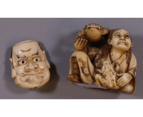 Japanese ivory netsuke of a seated man with two frogs, together with a carved ivory double headed mask head. (B.P. 21% + VAT)