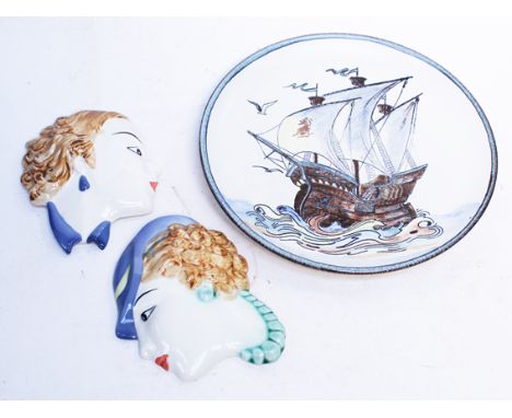 An Art Deco pottery charger and a pair of wall hanging masks