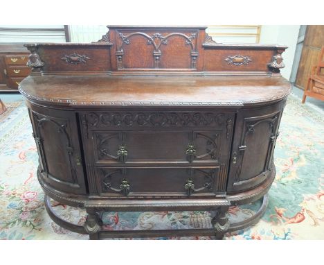 Heavily carved oak bow front serving cabinet with raised back with craved and panelled detail above bowed break front with tw