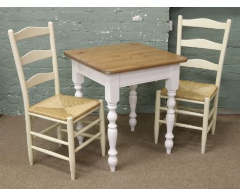 A white painted dining table with stripped pine top and two rush seat ladder back chairs.