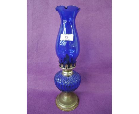 A vintage oil burner lamp with blue glass well and chimney