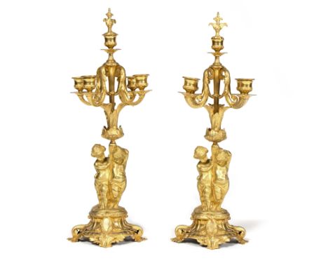 A pair of gilt metal four-branch five-light candelabra, with twin putto supports on oval bases with leaf-shaped feet, 56cm hi