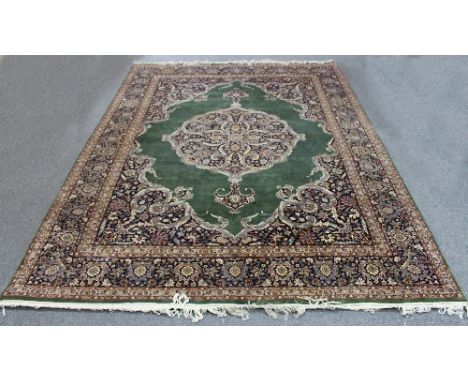 An Eastern style carpet with central medallion on a green ground within a figured floral border, 372cm x 272cm