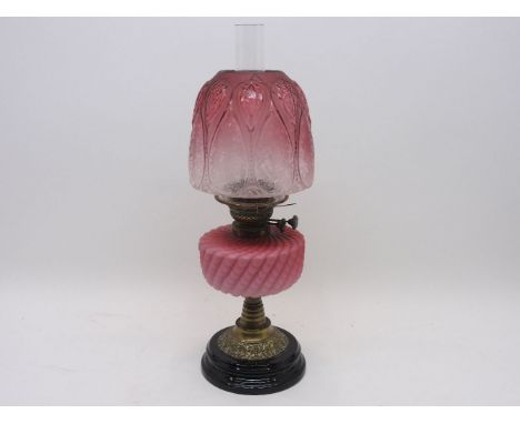 A Victorian brass oil lamp with enamel sunburst levers, having a graduated raspberry glass circular reservoir, raised on a ba