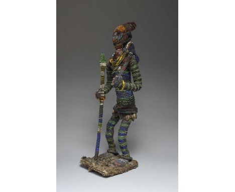A Yoruba beaded standing figureNigeriacoloured glass beads, cloth, cowrie shells and coconut discs, holding an axe in his lef
