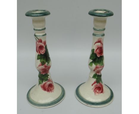 A PAIR OF LLANELLY CANDLESTICK HOLDERS with circular bases and decorated with tea-roses, stencilled mark to bases, 24cms high