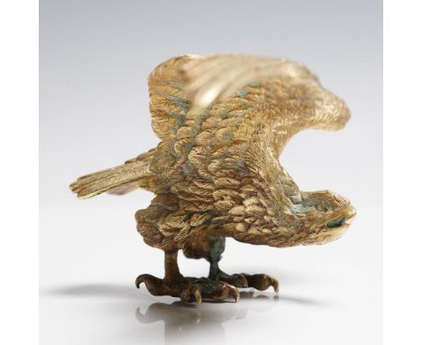 A cast bronze sculpture depicting a powerful eagle in mid-flight, descending with talons extended and clutching a small anima