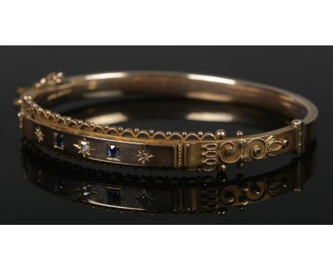 A vintage 9ct gold bangle set with three small diamonds and two sapphires. 9.88g.  