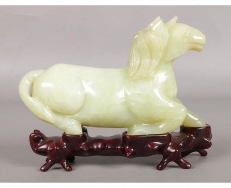 A Chinese carved jade figure of a recumbent horse, on hardwood stand. Length 14cm.  Tip of ear chipped.