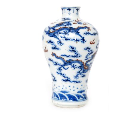 A Chinese Qing Dynasty 18th Century porcelain vase of baluster form hand painted in underglaze blue and red with dragons amon