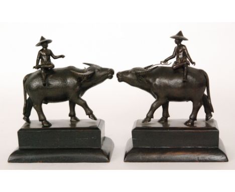 A pair of early 20th Century Burmese bronze figures of peasants each wearing a hat and sat astride a water buffalo, on square