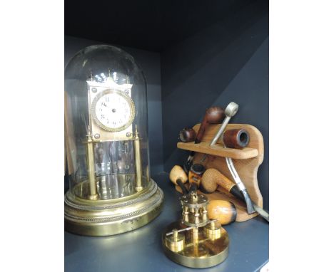 A vintage anniversary clock having glass dome and a selction of smoker's pipes on stand