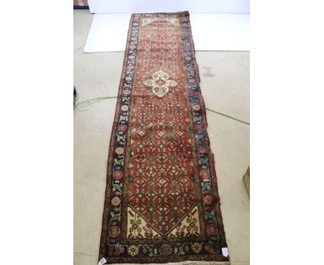 Large woven runner rug with red ground and pattern shape centre and blue floral border, W 75cm